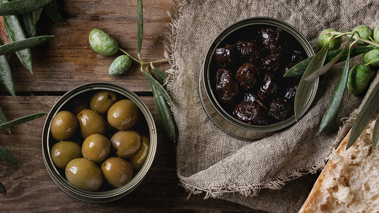 A top-down view of cans of green and black olives on a wooden surface
