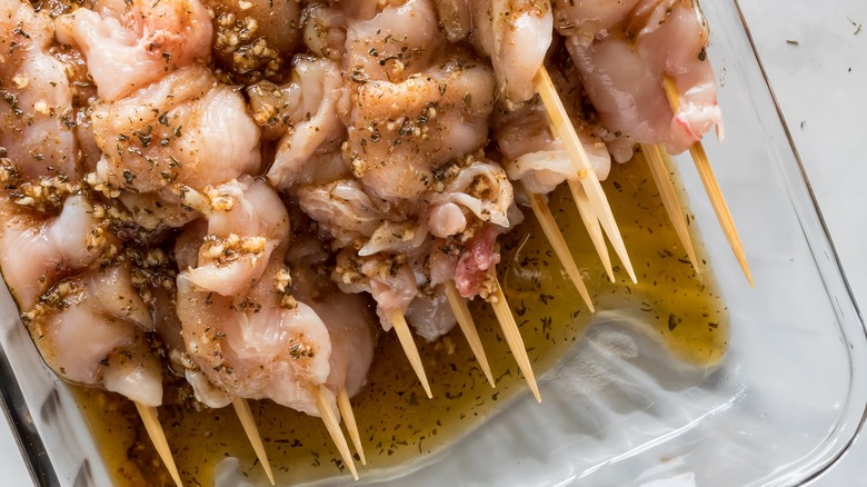 Raw chicken skewers in a glass dish of homemade herbs and spices marinade