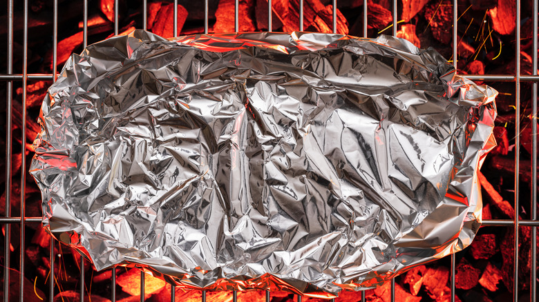 Food in aluminum foil cooking over hot BBQ coals