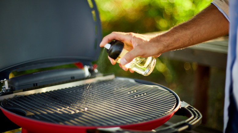 Close up of a man's hand spraying oil on barbecue