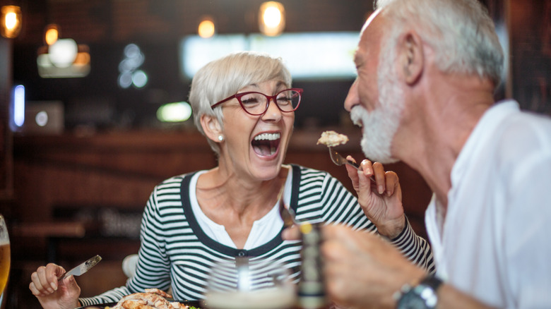 A woman jokingly feeding her partner at a restaurant