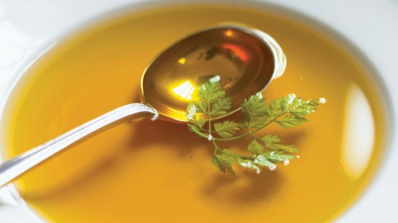 A bowl of consommé with a silver spoon and herb garnish