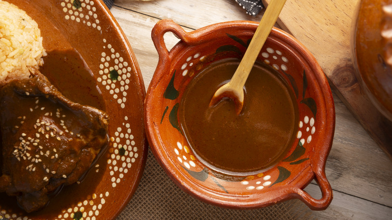 A bowl of mole poblano next to a plate of chicken and rice