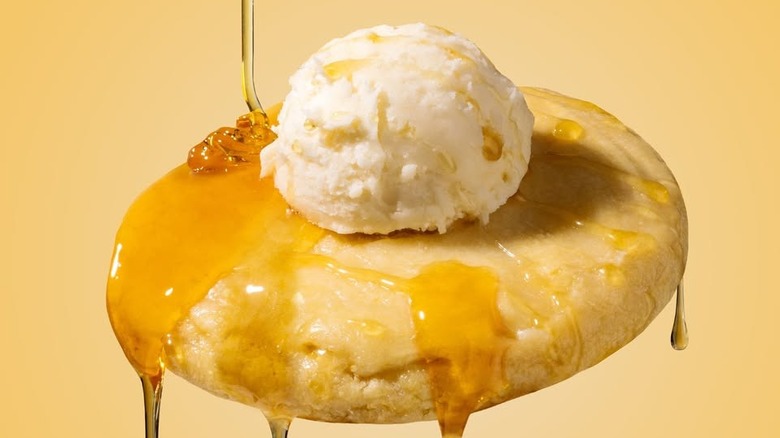 Crumbl Cornbread cookie with scoop of buttercream and drizzled with honey on yellow background