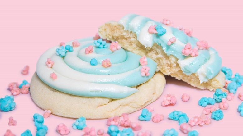 Two of Crumbl's Cotton Candy Cookies on pink background surrounded by blue and pink cotton candy pieces