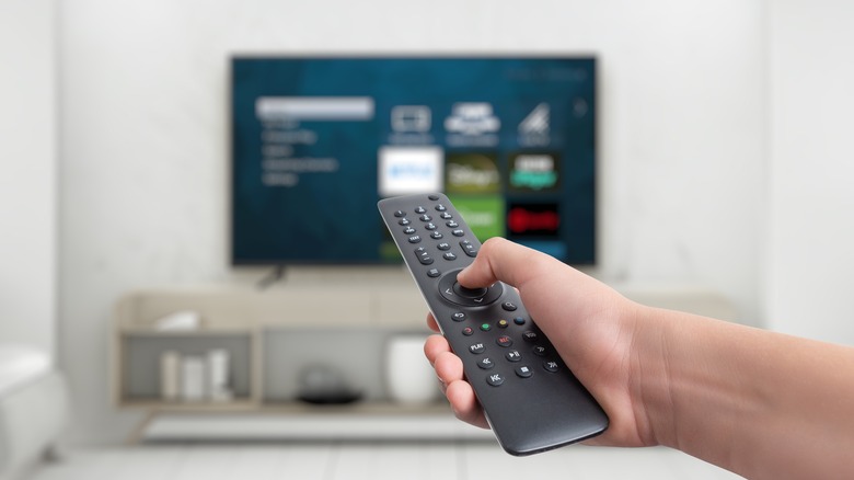 Hand holding a remote control in front of a TV