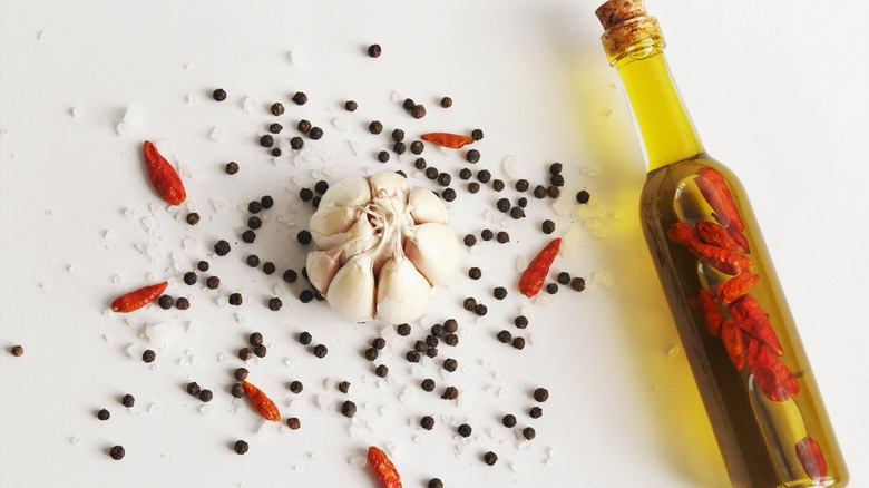 bottle of olive oil with chili beside peppercorns, chili flakes, and garlic