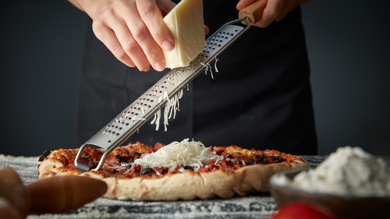 Cheese being grated onto pizza