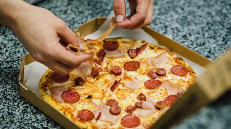 Person adding toppings to pizza