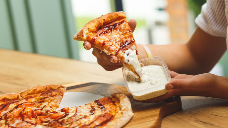 a girl dips a slice of pizza into a ranch dressing container