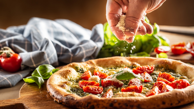hand spreading grated parmesan on pizza