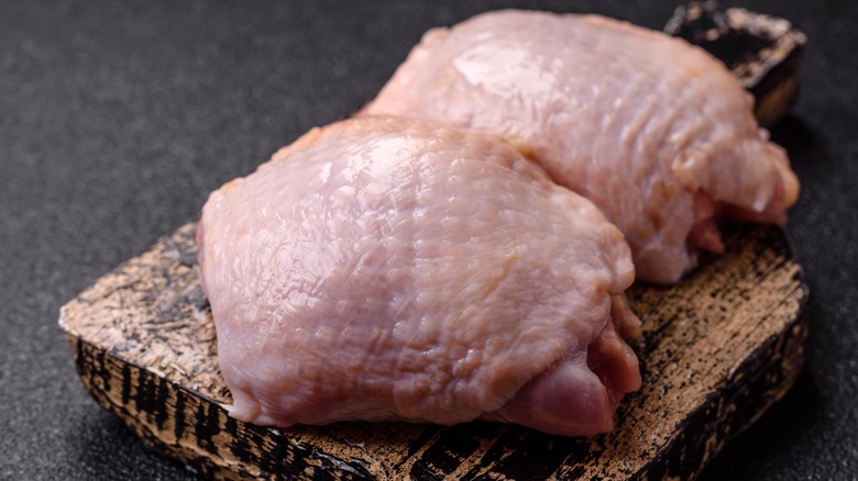 Two raw chicken thighs with skin on, on a wooden board