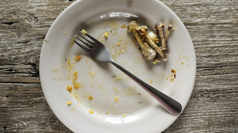 An empty plate and fork with several chicken thigh bones on one side