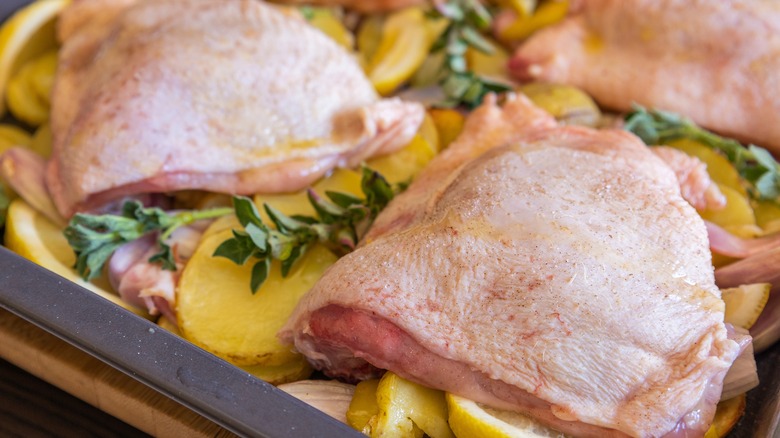 Close up of chicken thigh with potatoes, lemons, and shallot onions in a tray