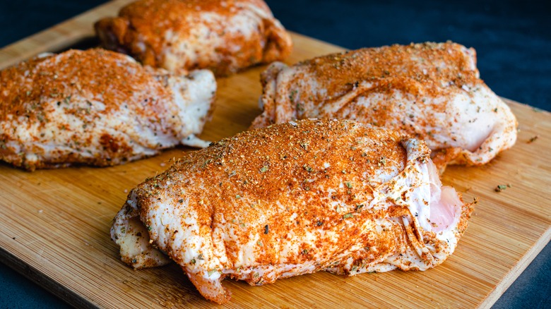Raw, spice-rubbed chicken thighs on a wooden cutting board