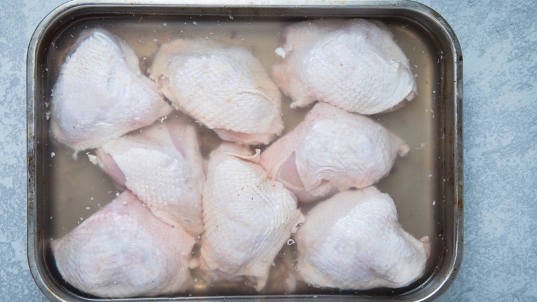 Chicken thighs being brined in a silver tin