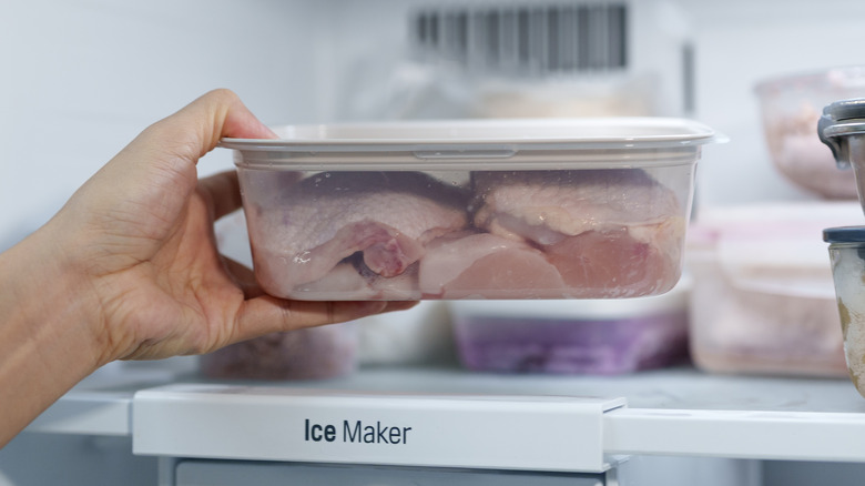 A hand taking a container of chicken thighs out of a fridge