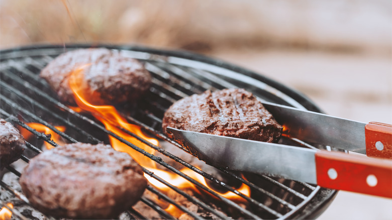 tongs grabbing burger on the grill