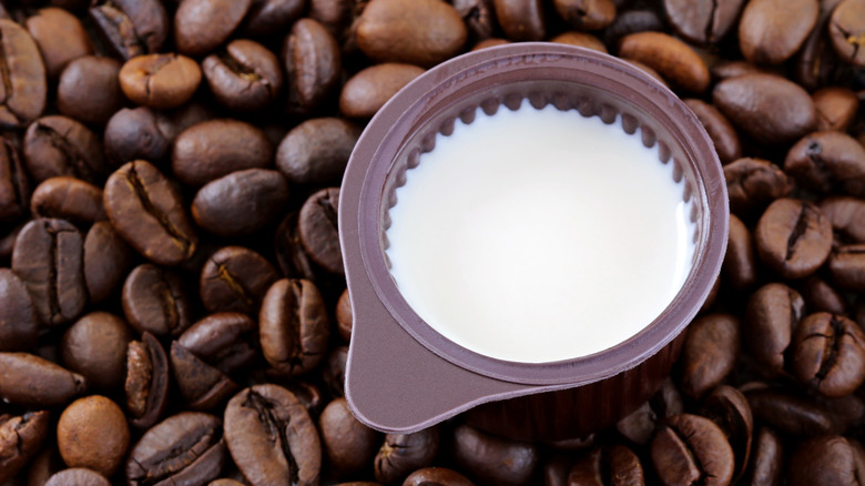 A small cup of coffee creamer on top of coffee beans
