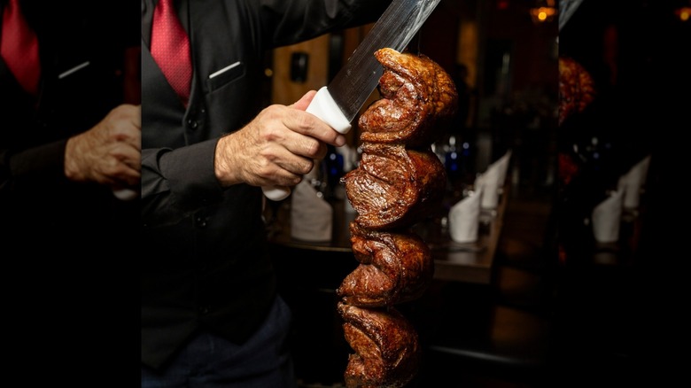 A Texas de Brazil waiter carves meat on a metal skewer