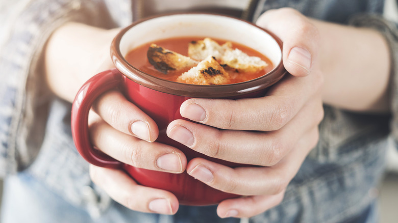 Hands holding a red cup of tomato soup
