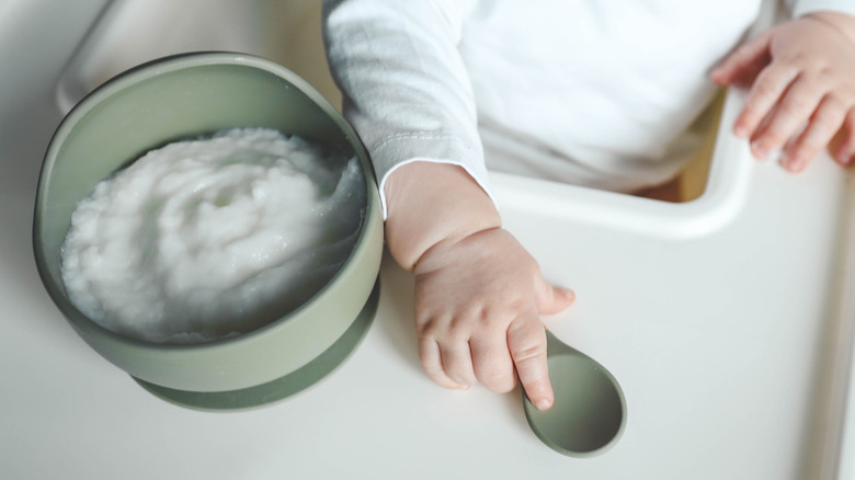 A baby in a high chair with a bowl of food on the tray
