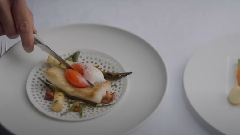 Hand with knife cutting into egg on plate