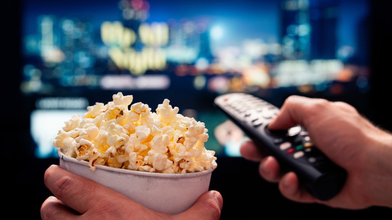 person watching TV with remote control and popcorn