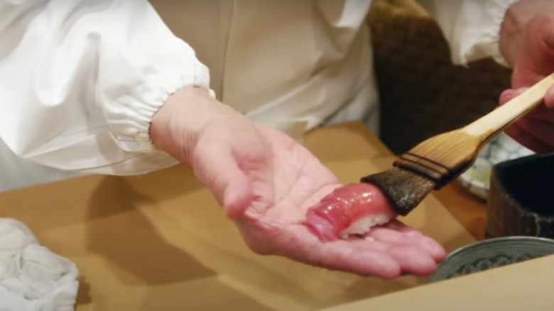 Hand delicately brushing a piece of sushi