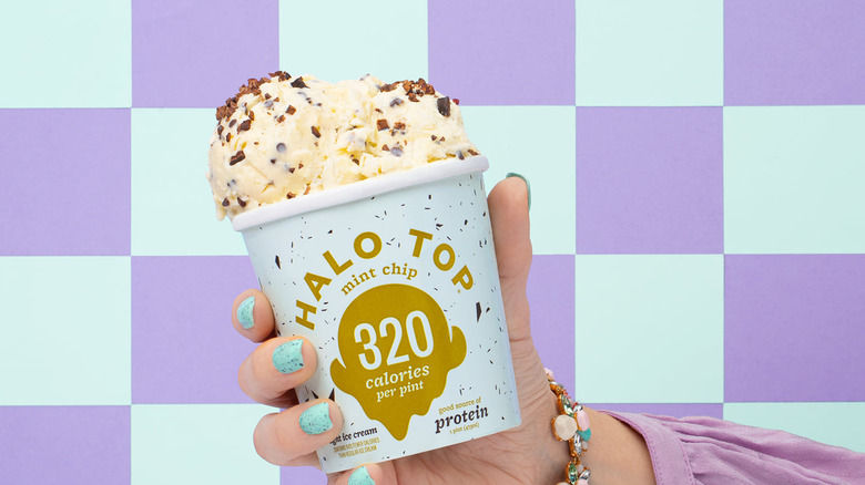 Hand holding container of Halo Top Mint Chip in front of checkered background