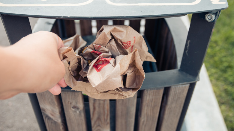 A hand putting a crumpled up McDonald's bag in a trash can