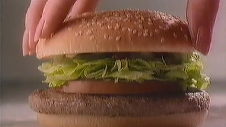 A woman putting the top bun on a McDonald's Mclean Deluxe hamburger