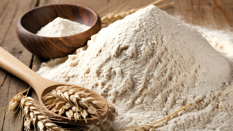 A pile of flour next to ears of wheat on a spoon