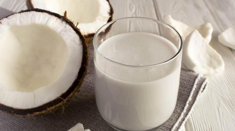 A glass of coconut milk next to two halves of coconut