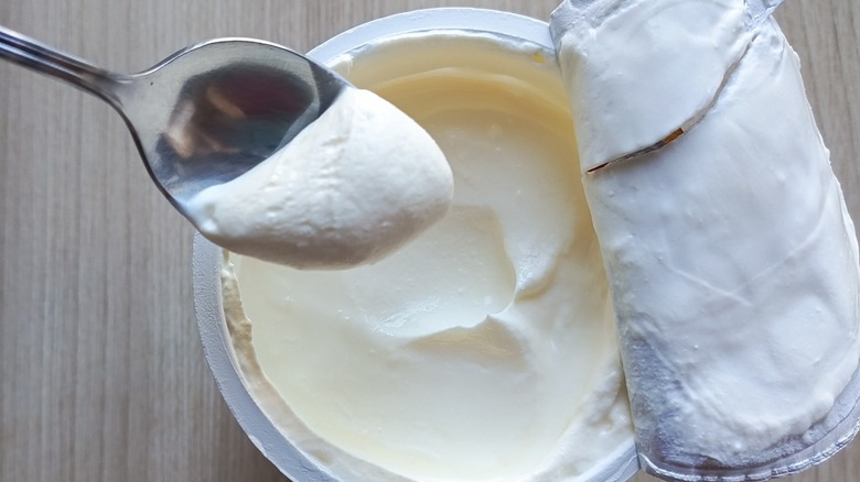 A spoon taking out sour cream from an opened tub