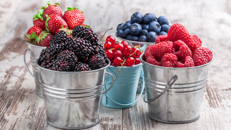 Fresh berries in tin cans on a rustic wooden table
