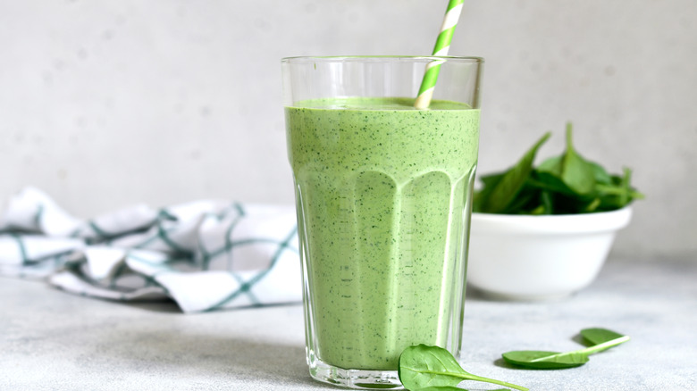 Spinach smoothie in a tall glass on white slate
