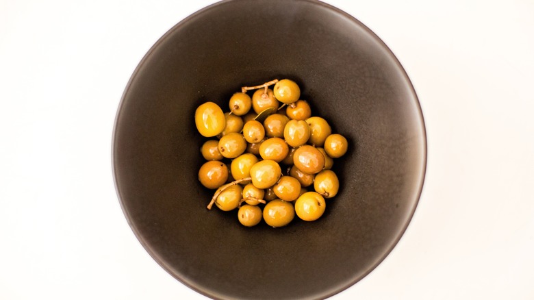 A bowl filled with arbequina olives, a staple in Spanish cuisine, against a white background.