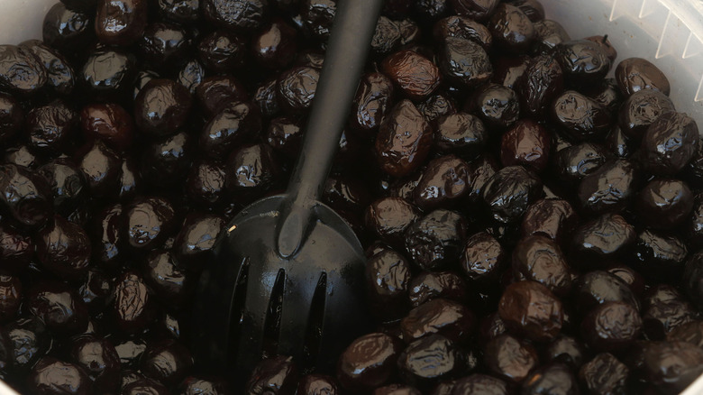 Black Beldi olives in a bucket with a serving spoon