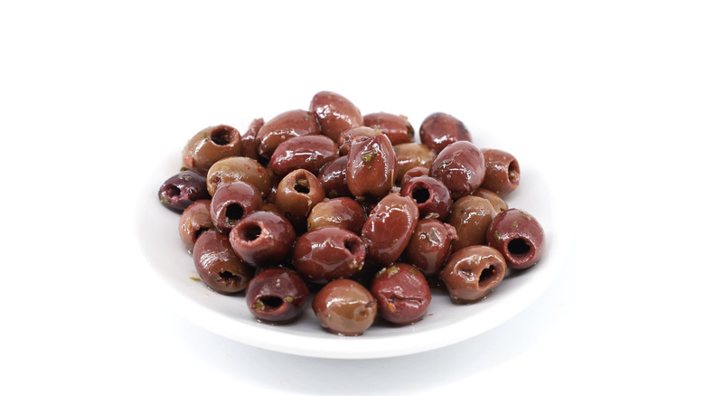 Seasoned pitted red olives of Leccino cultivar variety in a white ceramic appetizer plate. White background