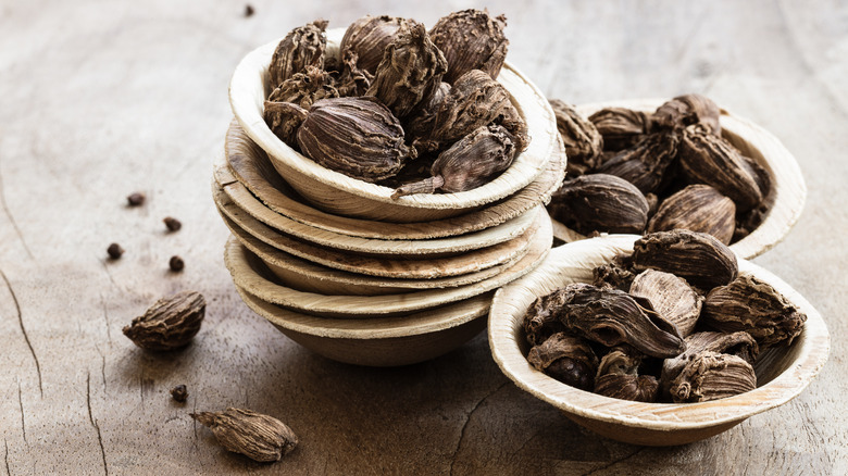Stacked-up bowls of black cardamom pods on a wooden table