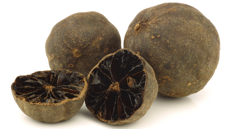 Two whole black limes and one cut in half on a white background