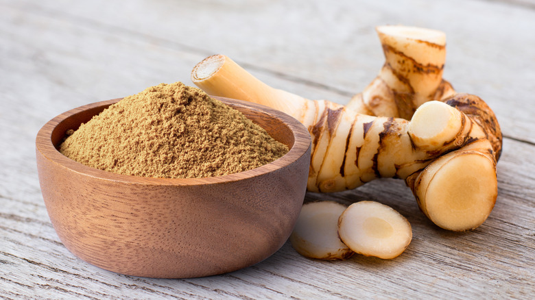Galangal poweder in a bowl next to a fresh root