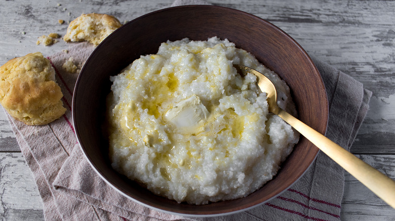 A bowl of grits with a gold spoon in it, next to biscuits