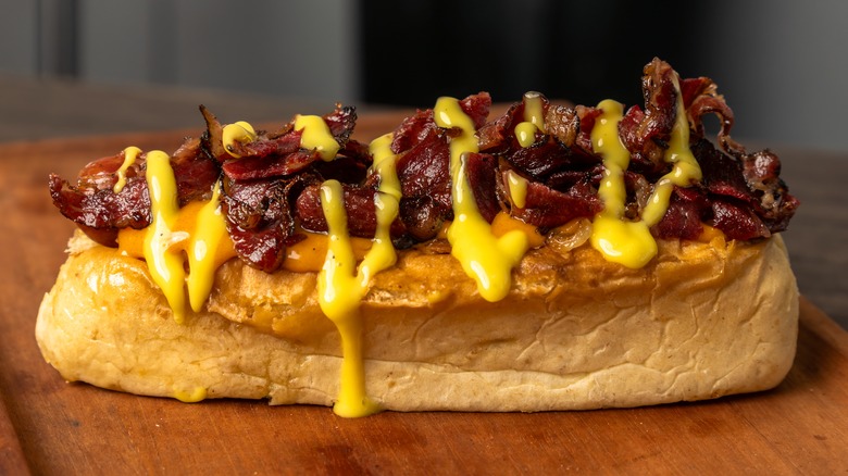 A hot dog topped with smoked beef and drizzled with honey mustard sauce