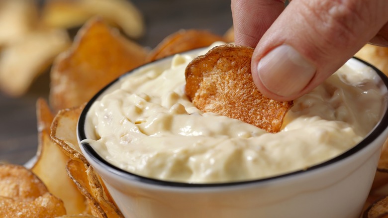 Close up person dipping potato chip into bowl of onion dip