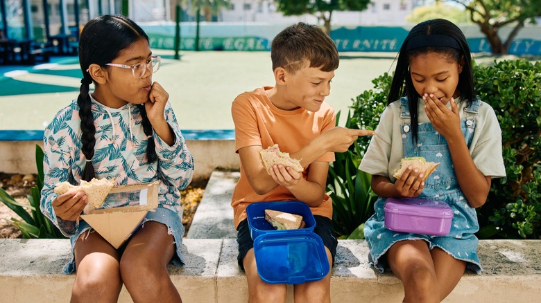 three children eat lunches from lunchboxes
