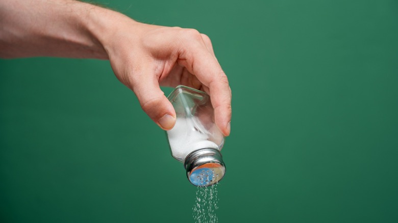 a hand pours table salt from a shaker