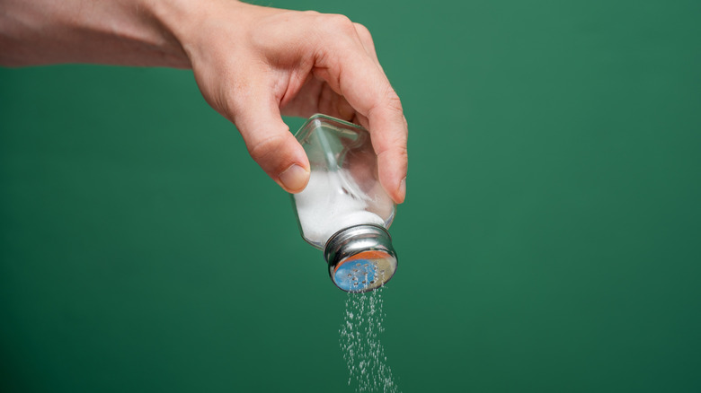 Hand shaking salt from a shaker, green background