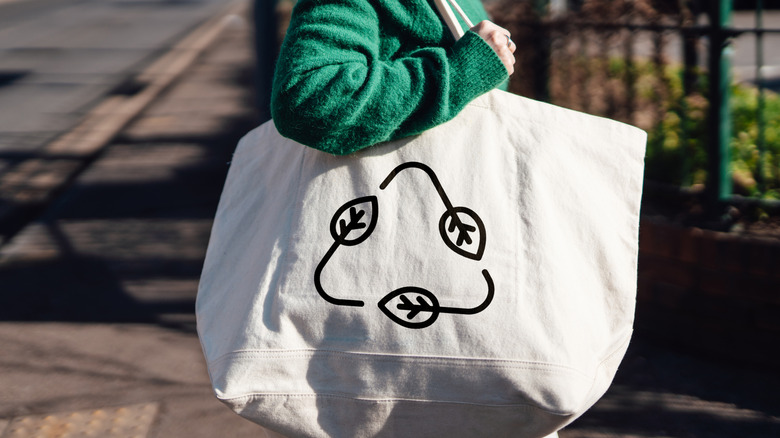 A shot of someone carrying a reusable canvas bag with a recycling symbol on it